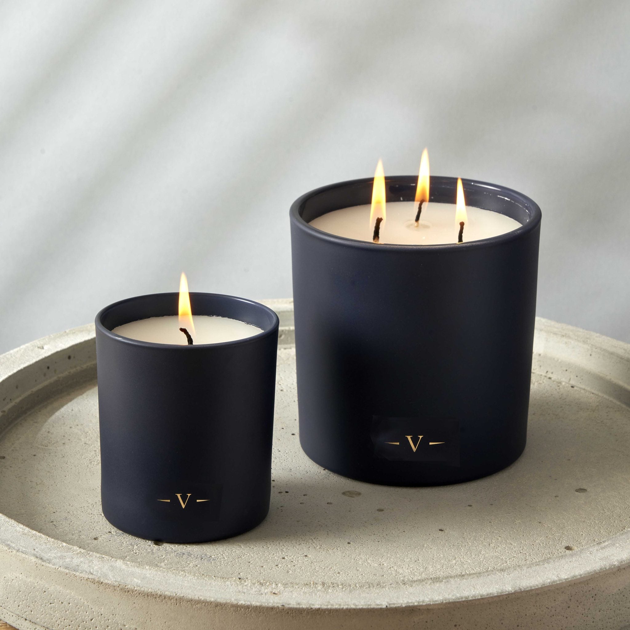 Two dark blue candles with a flame on a stone surface against a gray background