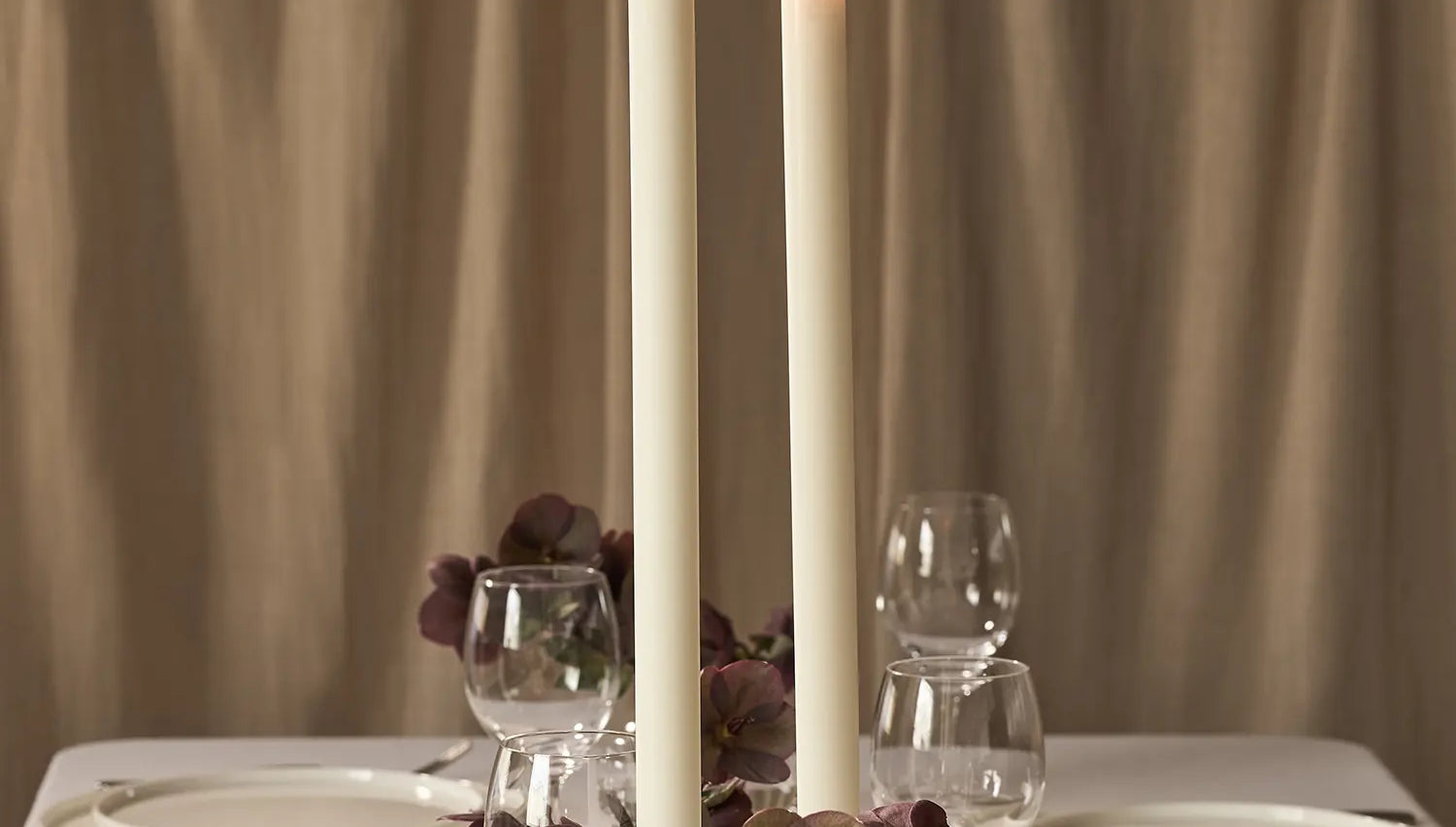 Two lit dining candles on a dining table.