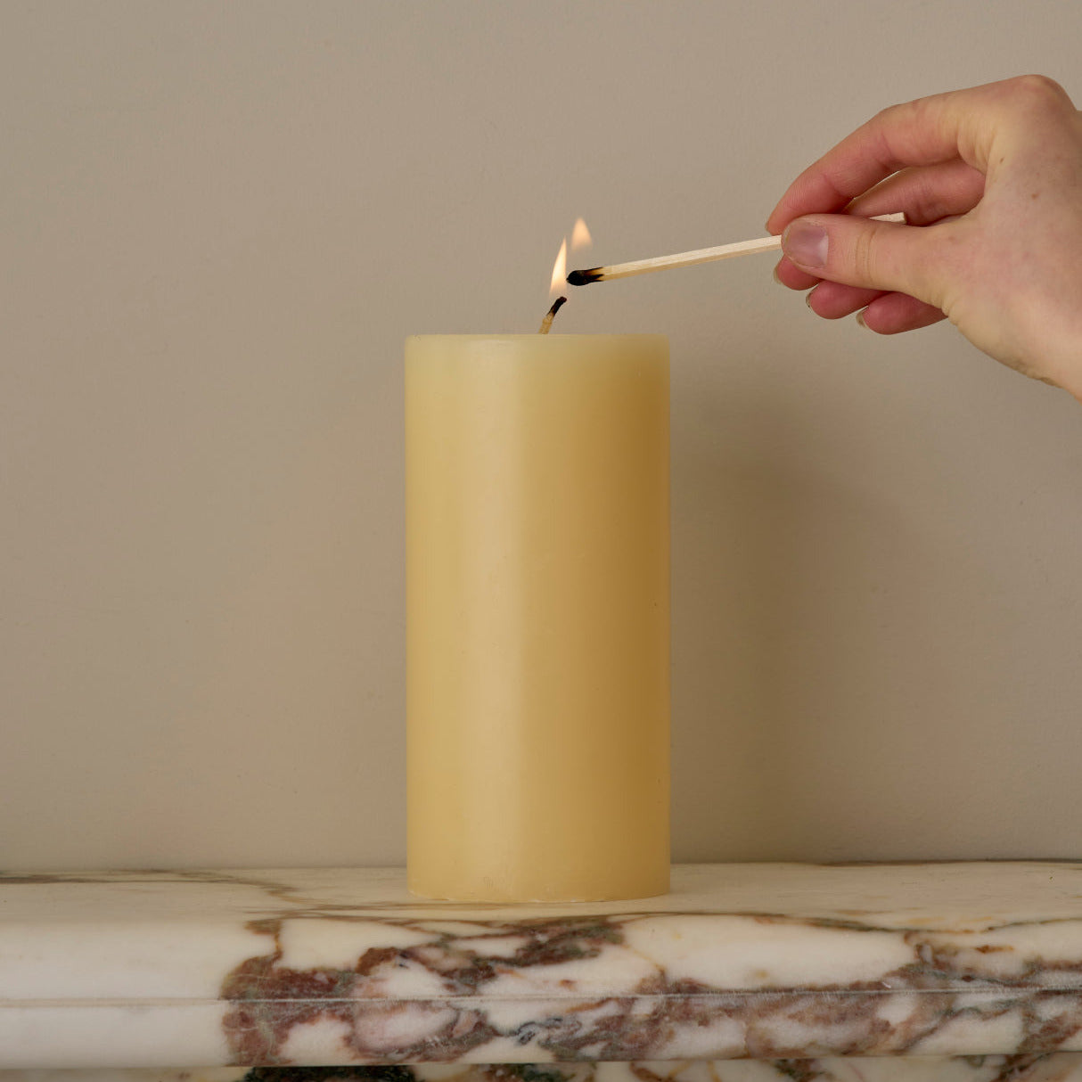 Hand lighting a yellow candle with a match on a marble surface.