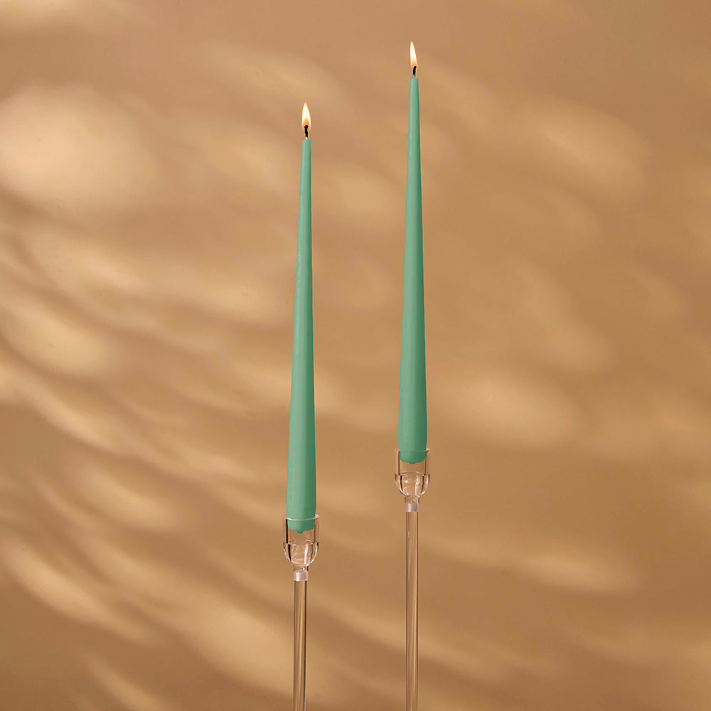 Two green candles with clear holders on a brown background