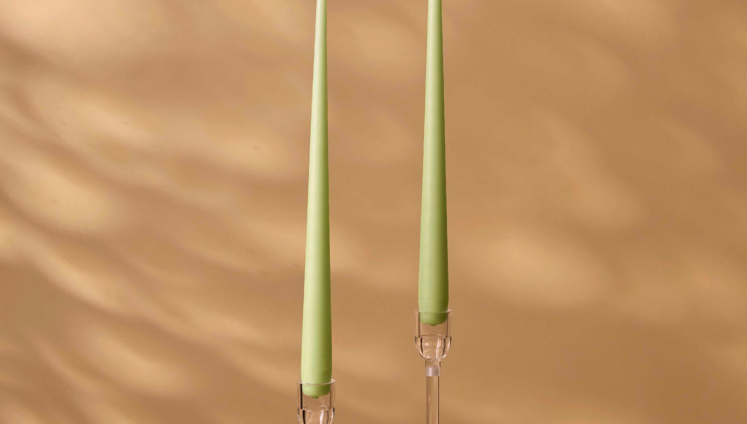 Two green candles in clear candle holders on a wooden surface with a beige wall background