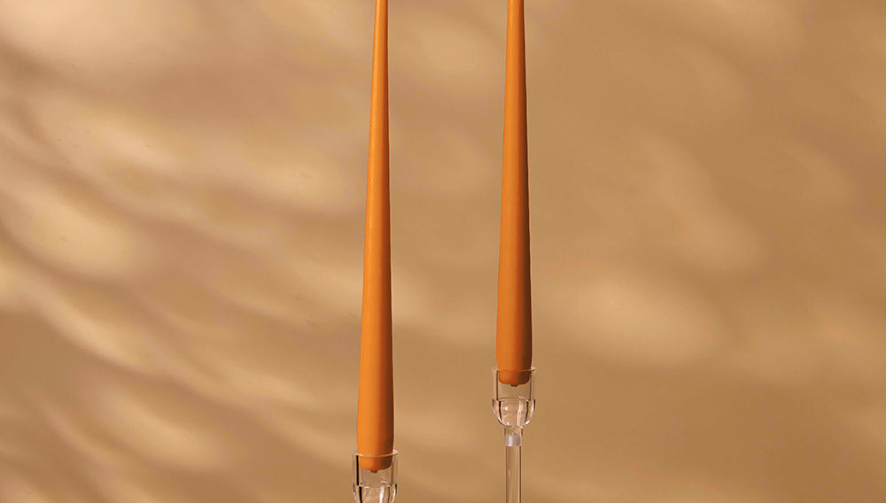 Two tall, orange candles with clear holders on a beige background