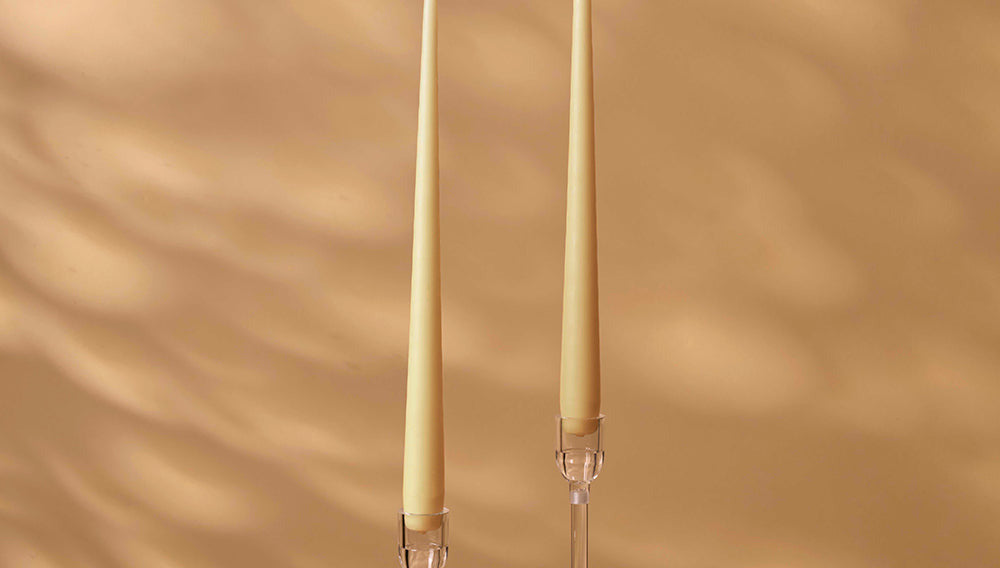 Two tall, thin candles with clear holders on a beige background