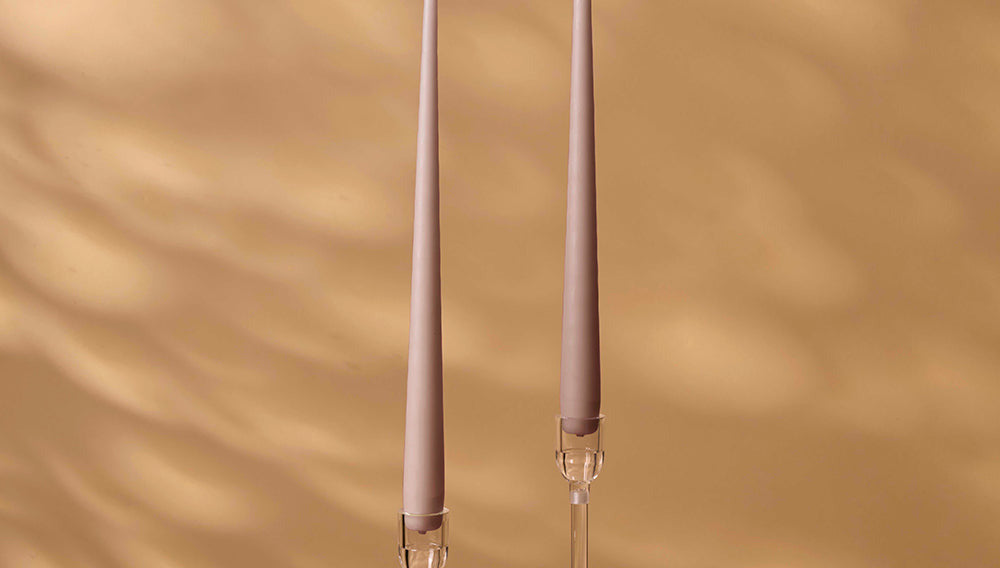 Two tall, thin candles with clear holders on a beige background
