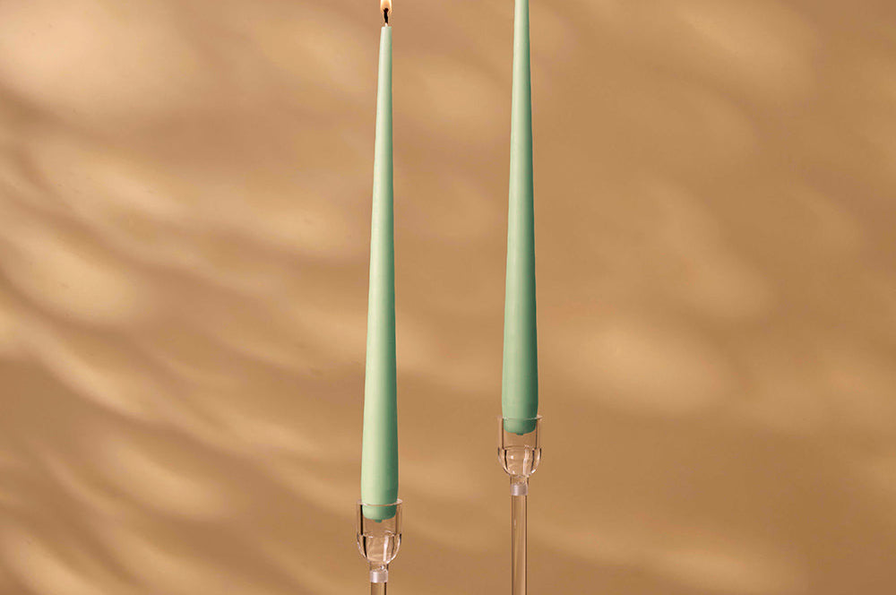 Two green candles with clear holders on a beige background