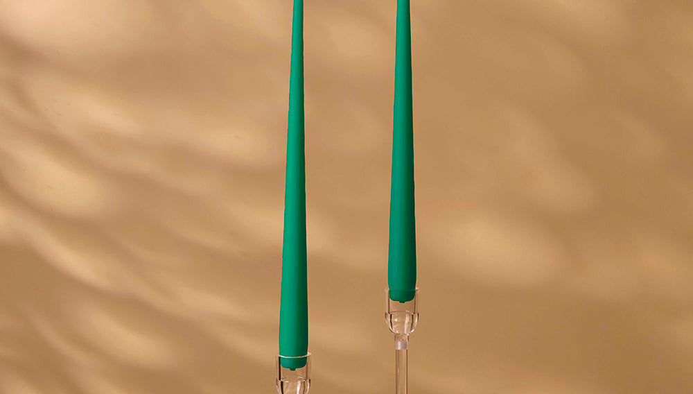 Two green candles with clear holders on a beige background