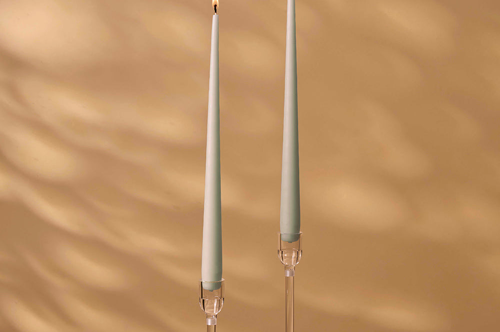 Two tall candle holders with lit candles on a beige wall background