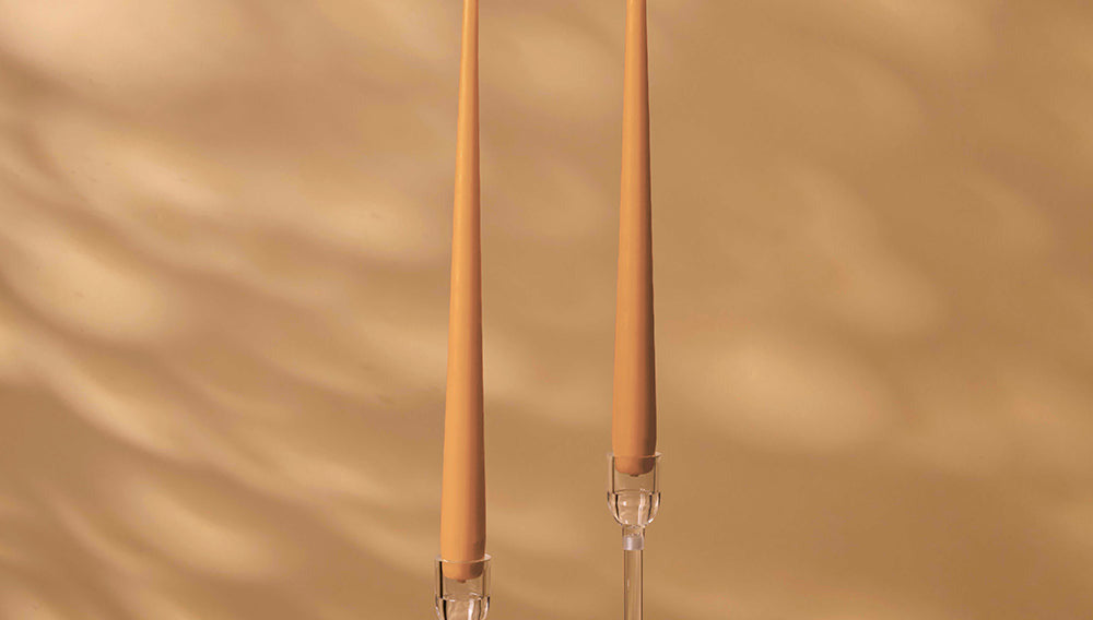 Two tall, thin candles with clear holders on a beige background