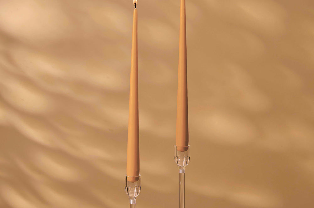 Two tall, thin candles with clear holders on a beige background
