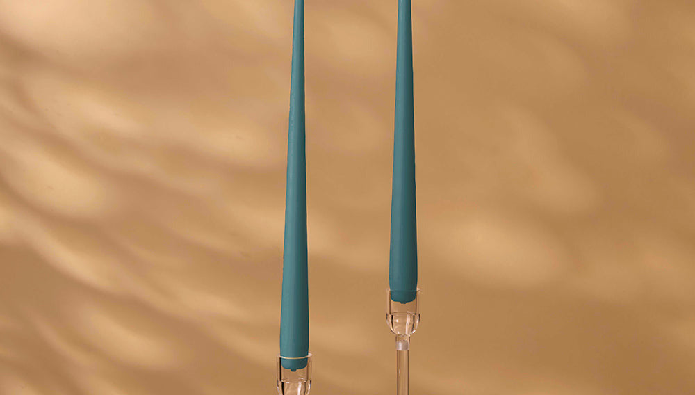 Two teal candles in clear candle holders with a beige background