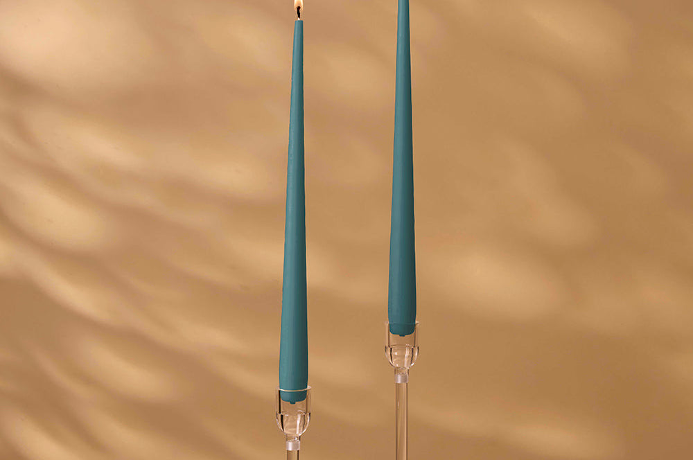 Two teal candles in clear candle holders with a beige background