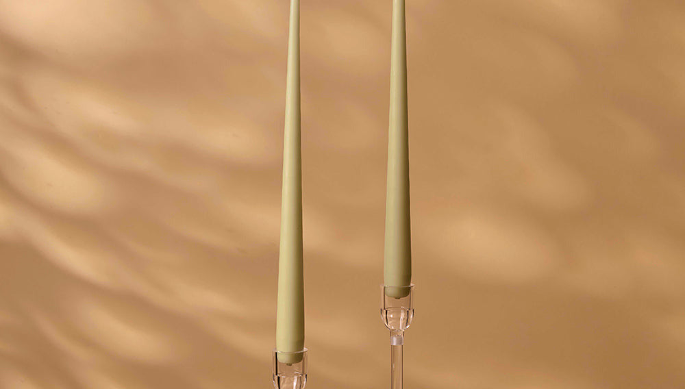 Two green candles with clear holders on a beige background