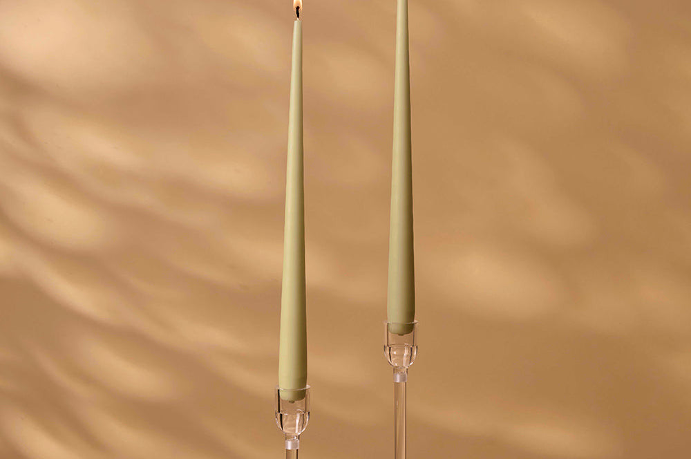 Two green candles with clear holders on a beige background