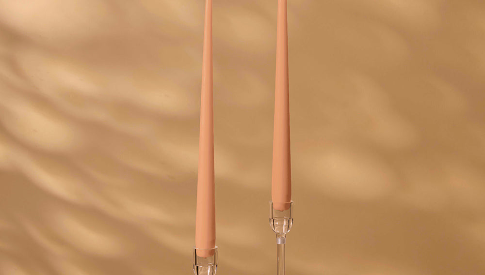Two peach-colored candles with clear holders on a beige background