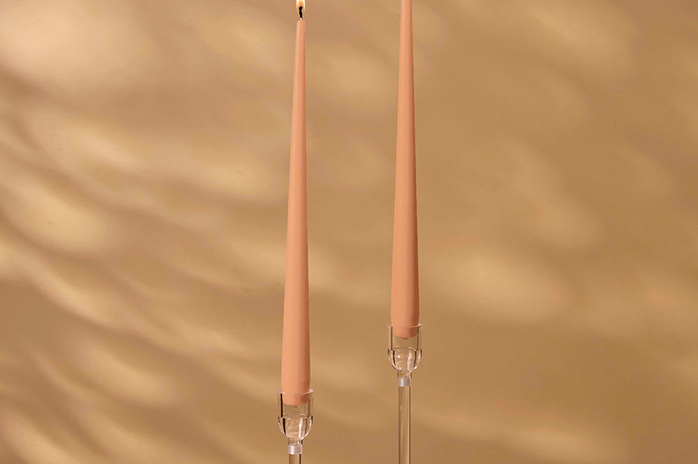 Two peach-colored candles with clear holders on a beige background