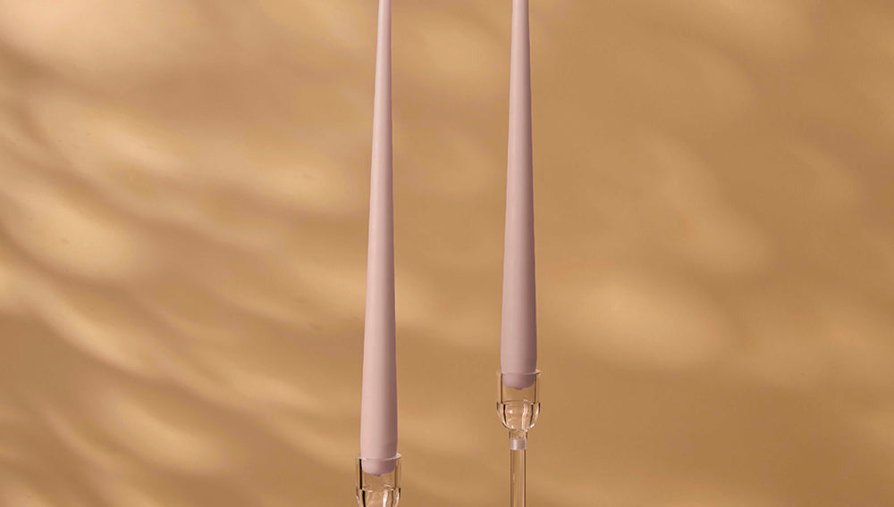Two tall, thin candles with decorative holders on a warm brown background