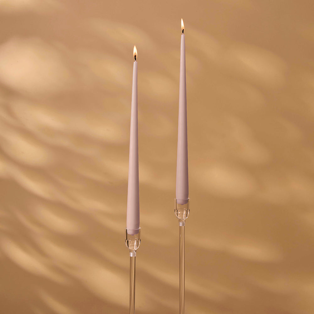 Two tall, thin candles with decorative holders on a warm brown background