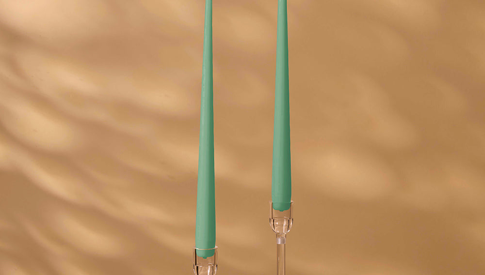 Two green candles with clear holders on a brown background