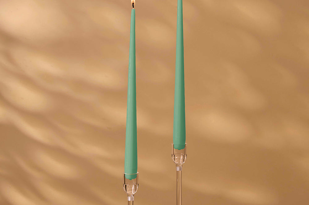 Two green candles with clear holders on a brown background
