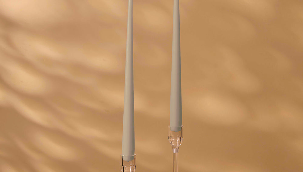 Two tall, thin candles with decorative holders on a warm brown background