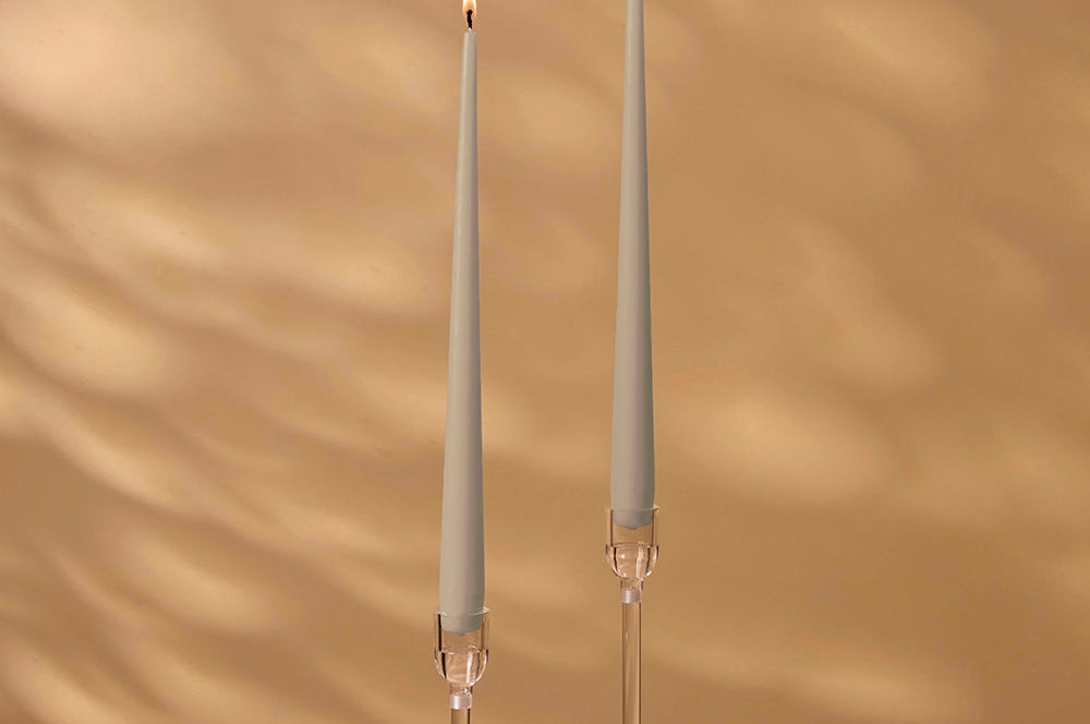 Two tall, thin candles with decorative holders on a warm brown background