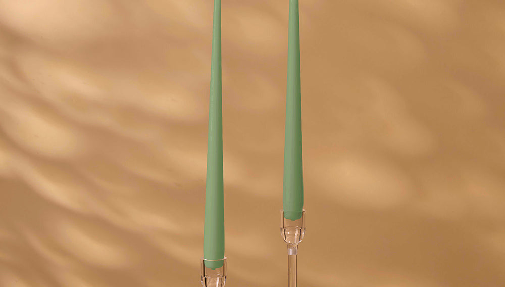 Two green candles with clear holders on a brown background