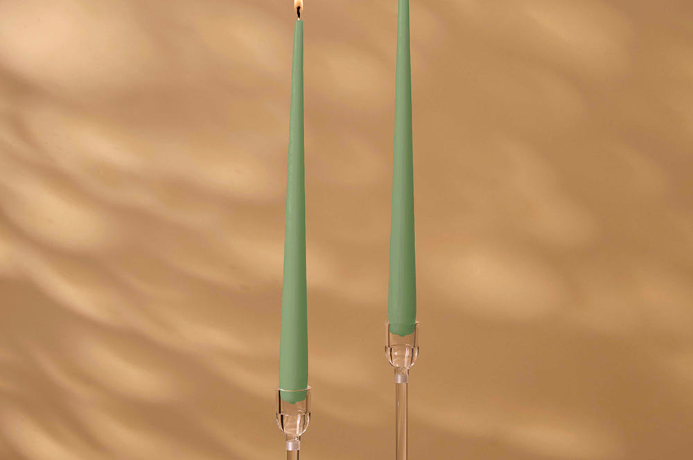 Two green candles with clear holders on a brown background