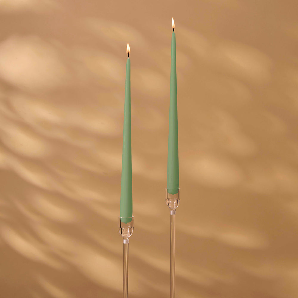 Two green candles with clear holders on a brown background