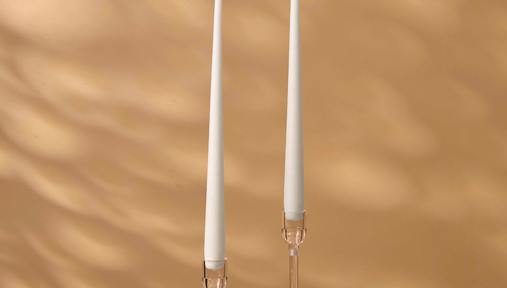 Two white candles with candle holders on a brown background