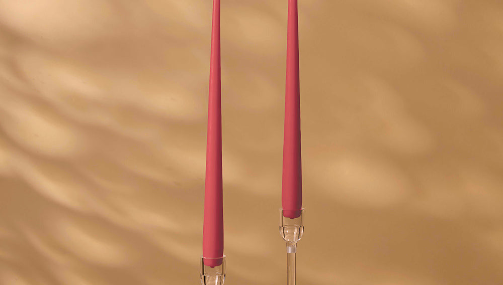 Two pink candles on clear candlesticks against a beige wall.