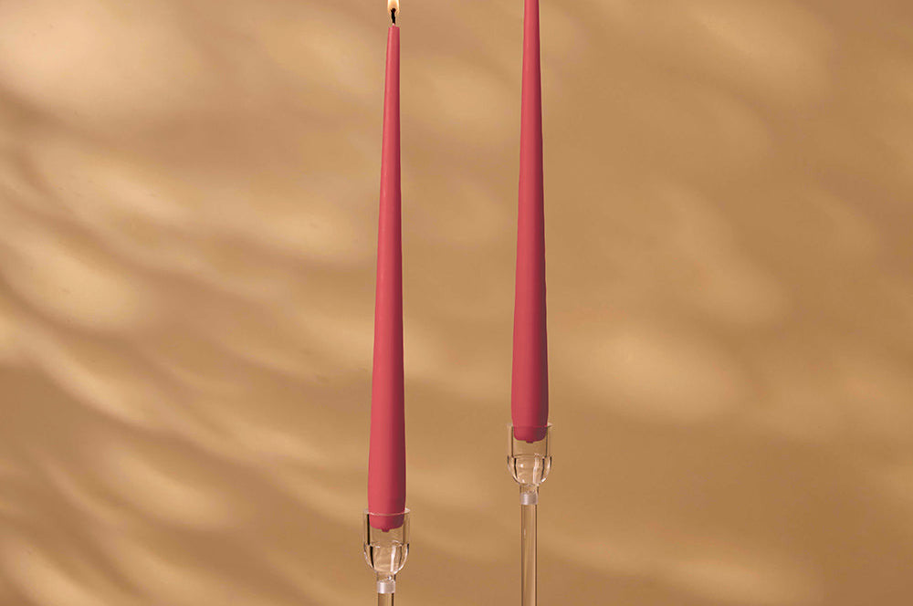 Two pink candles on clear candlesticks against a beige wall.