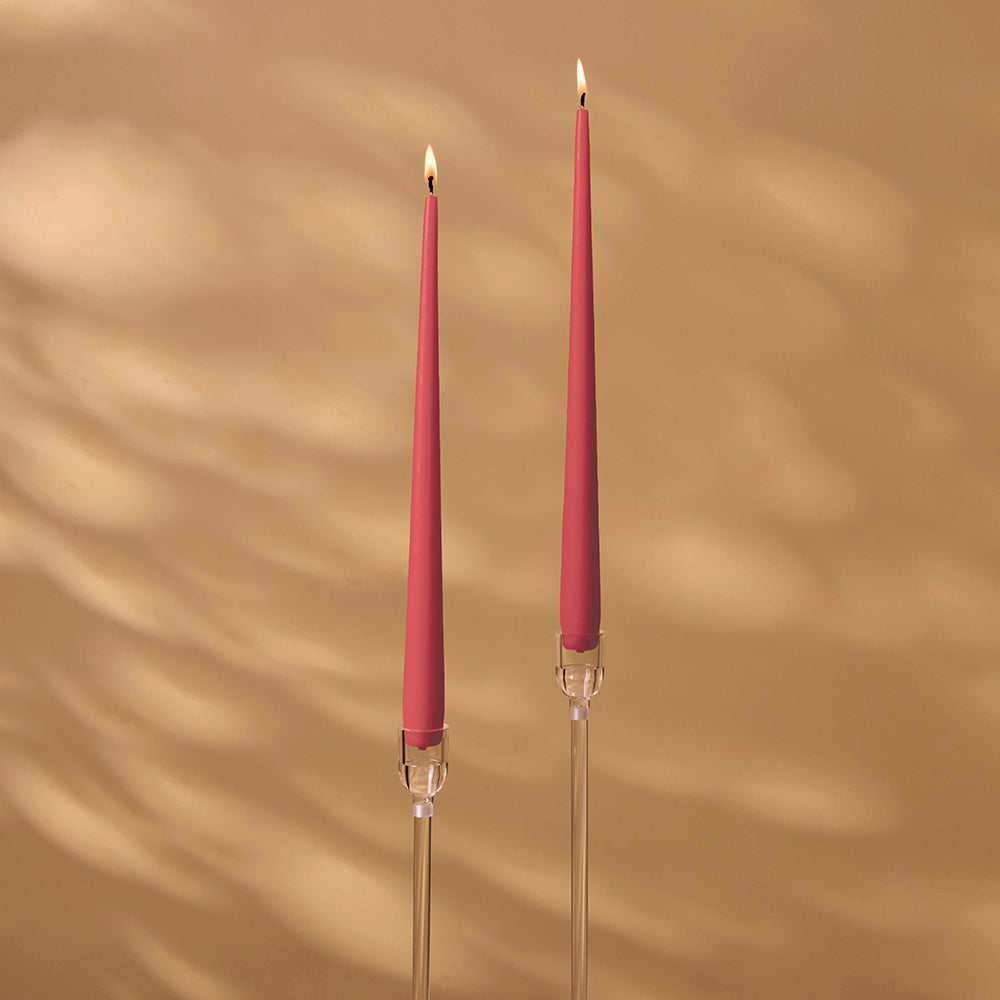 Two pink candles on clear candlesticks against a beige wall.