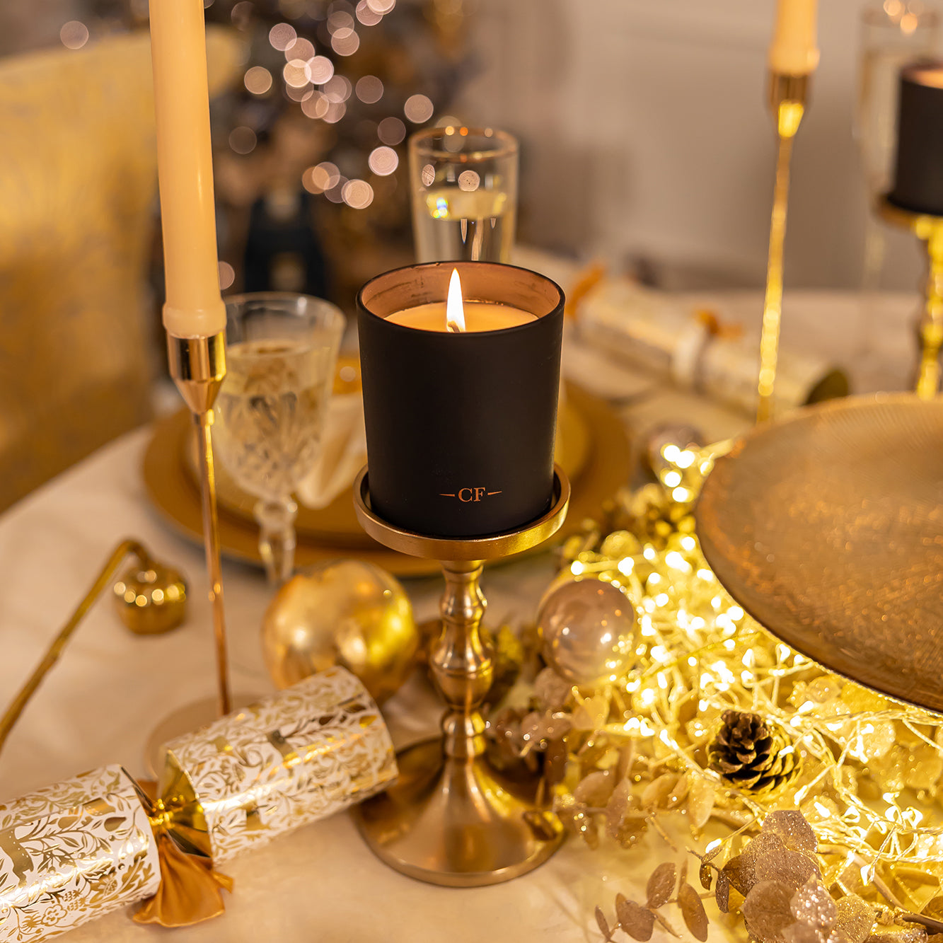 Decorative table setting with a lit candle in a black holder, surrounded by gold and silver ornaments.