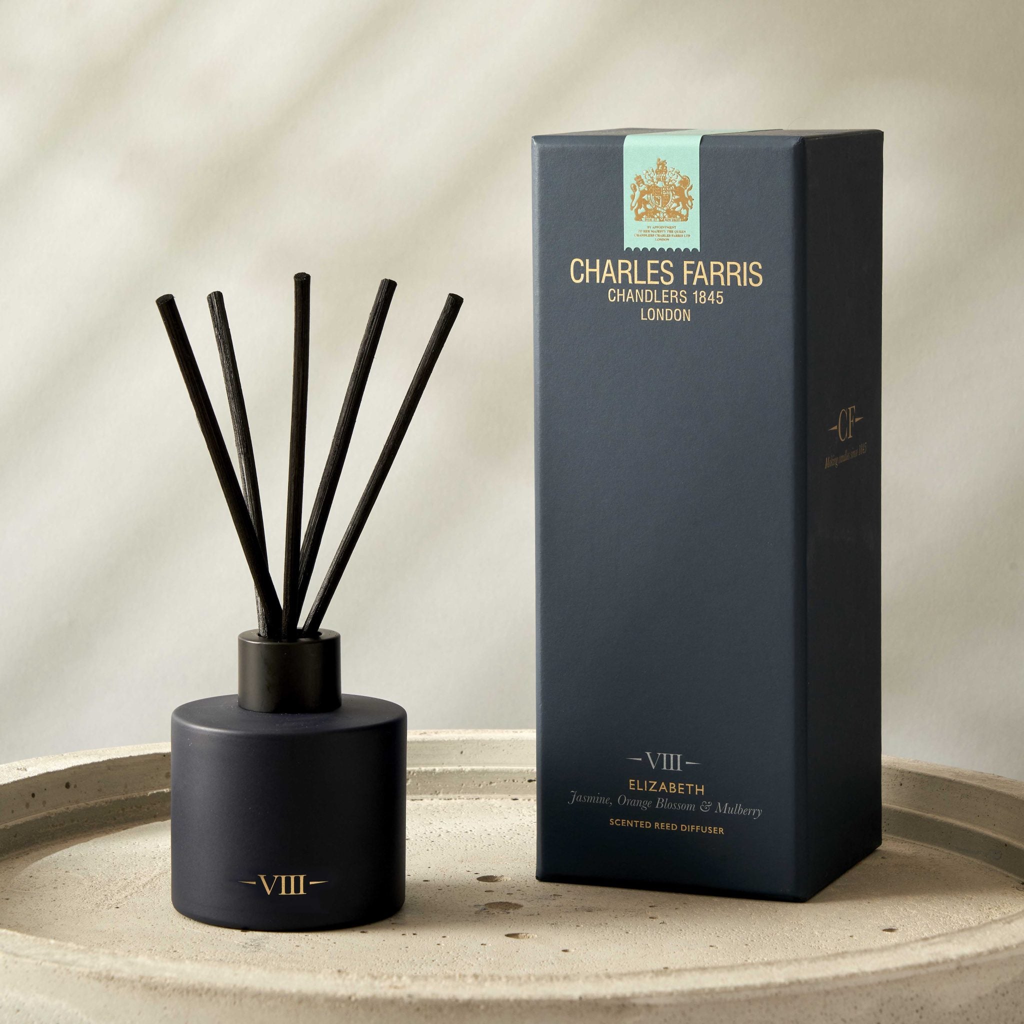 Reed diffuser with black sticks and its packaging on a beige surface