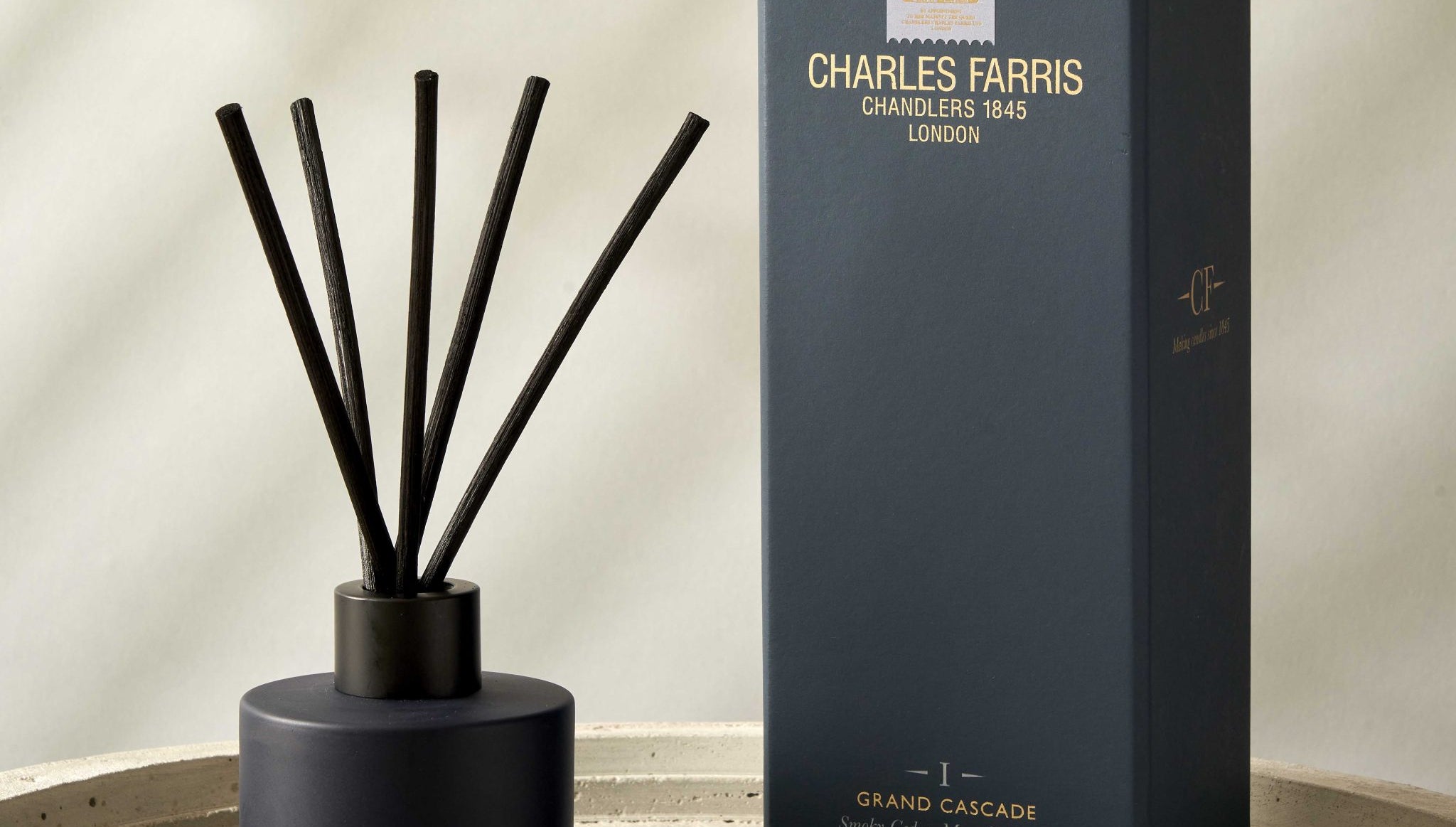 Black diffuser with sticks and its packaging on a beige surface