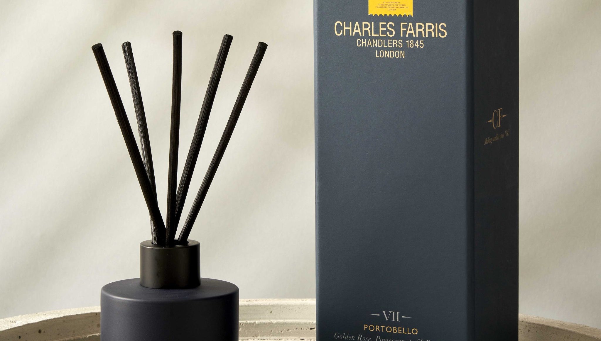 Dark blue Portobello reed diffuser with sticks and its packaging on a concrete surface