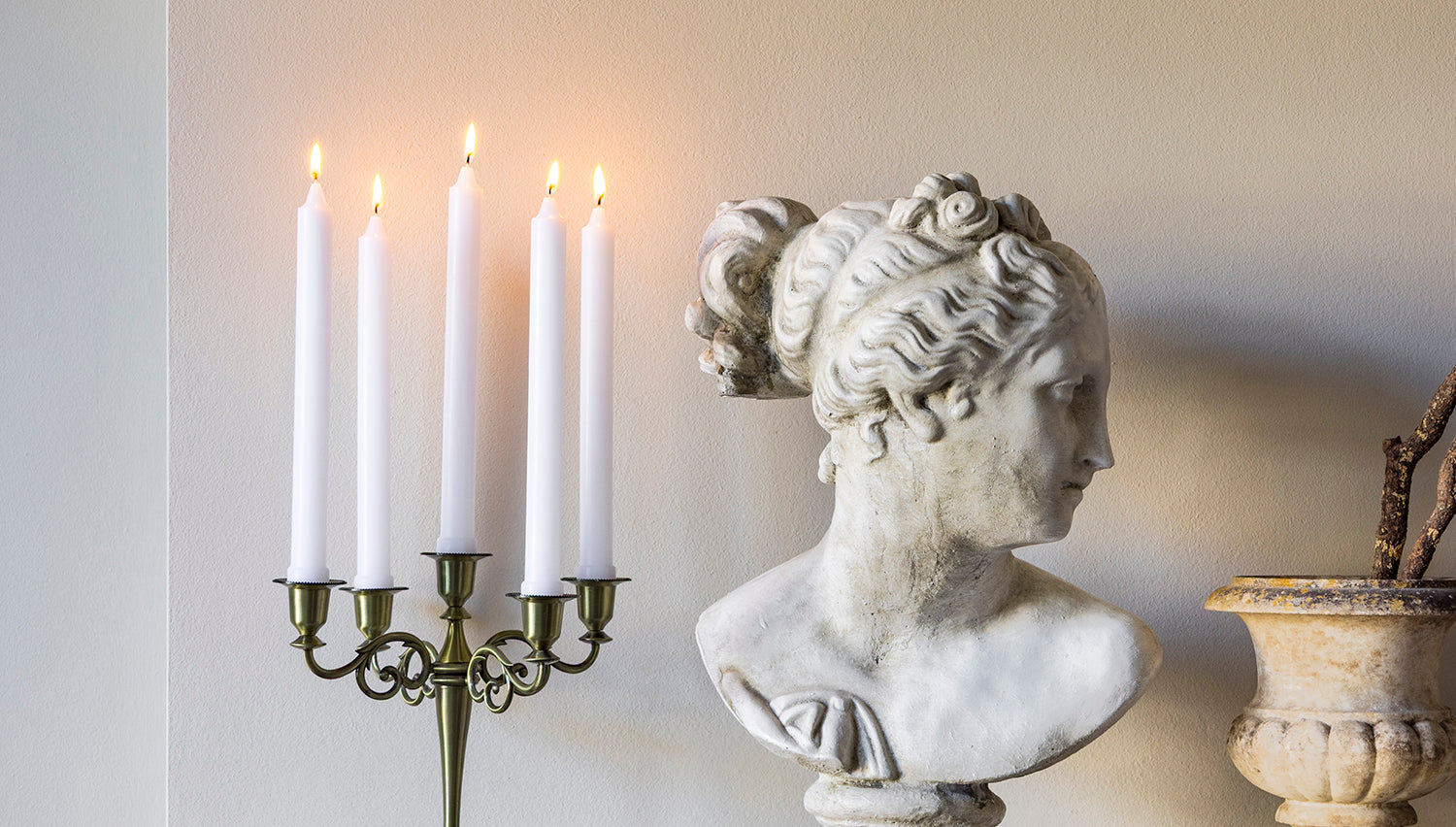 Bust of a classical figure, candle holder with lit candles, and decorative urn on a marble surface.