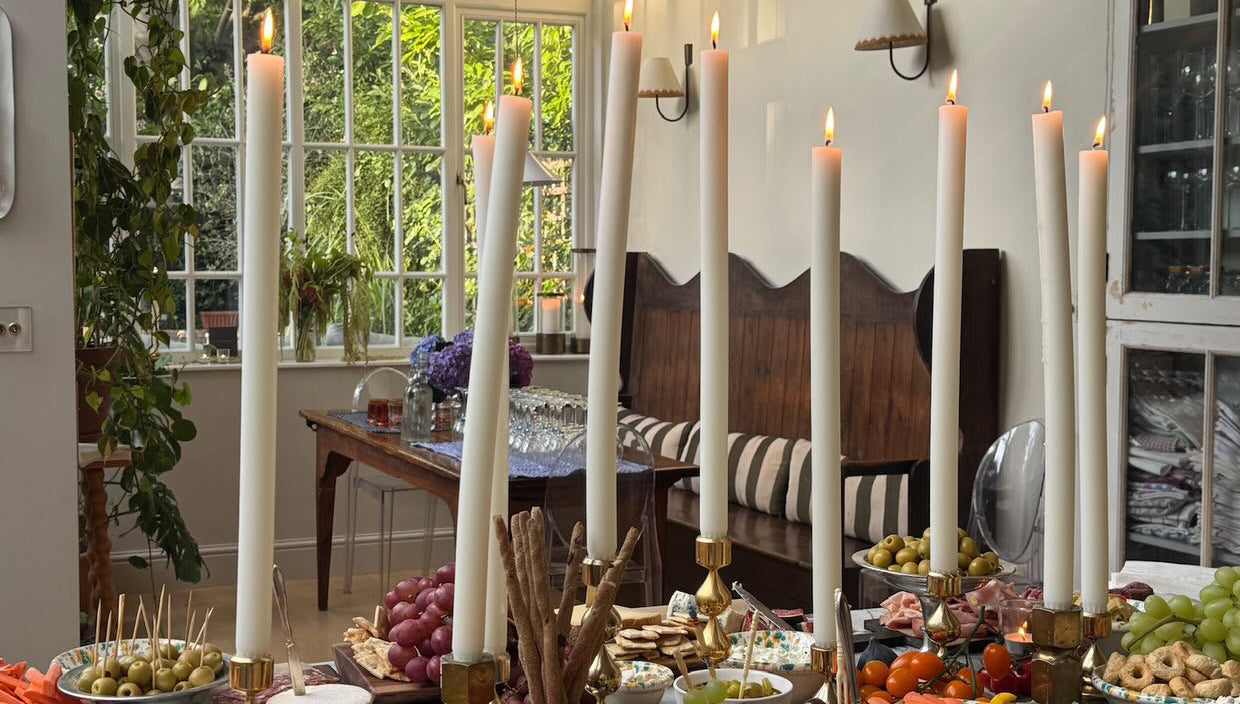 Dining room with a table set for a meal featuring dining candles, fruits, vegetables, and bread.