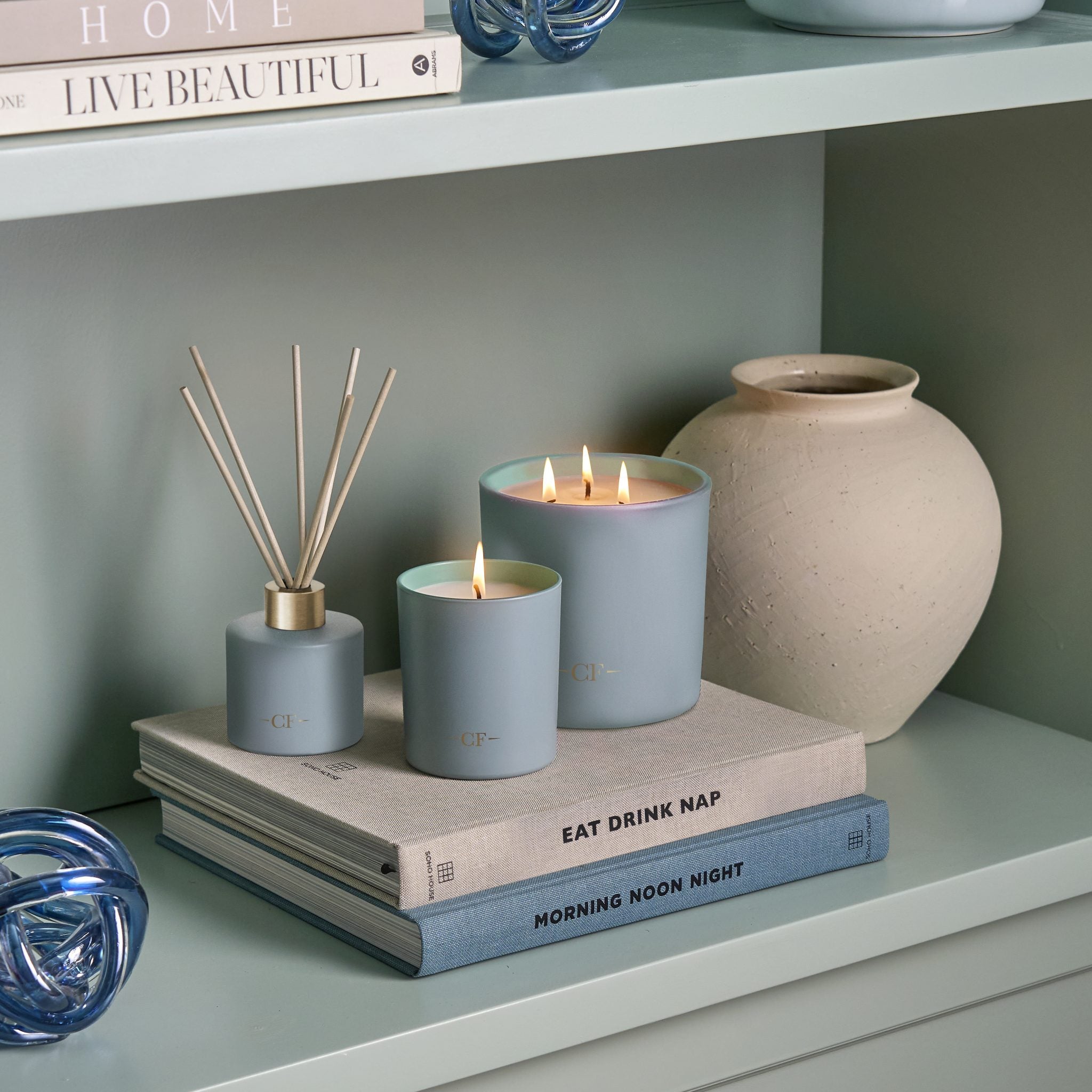 Decorative items including candles and a diffuser on a shelf with books and a vase.