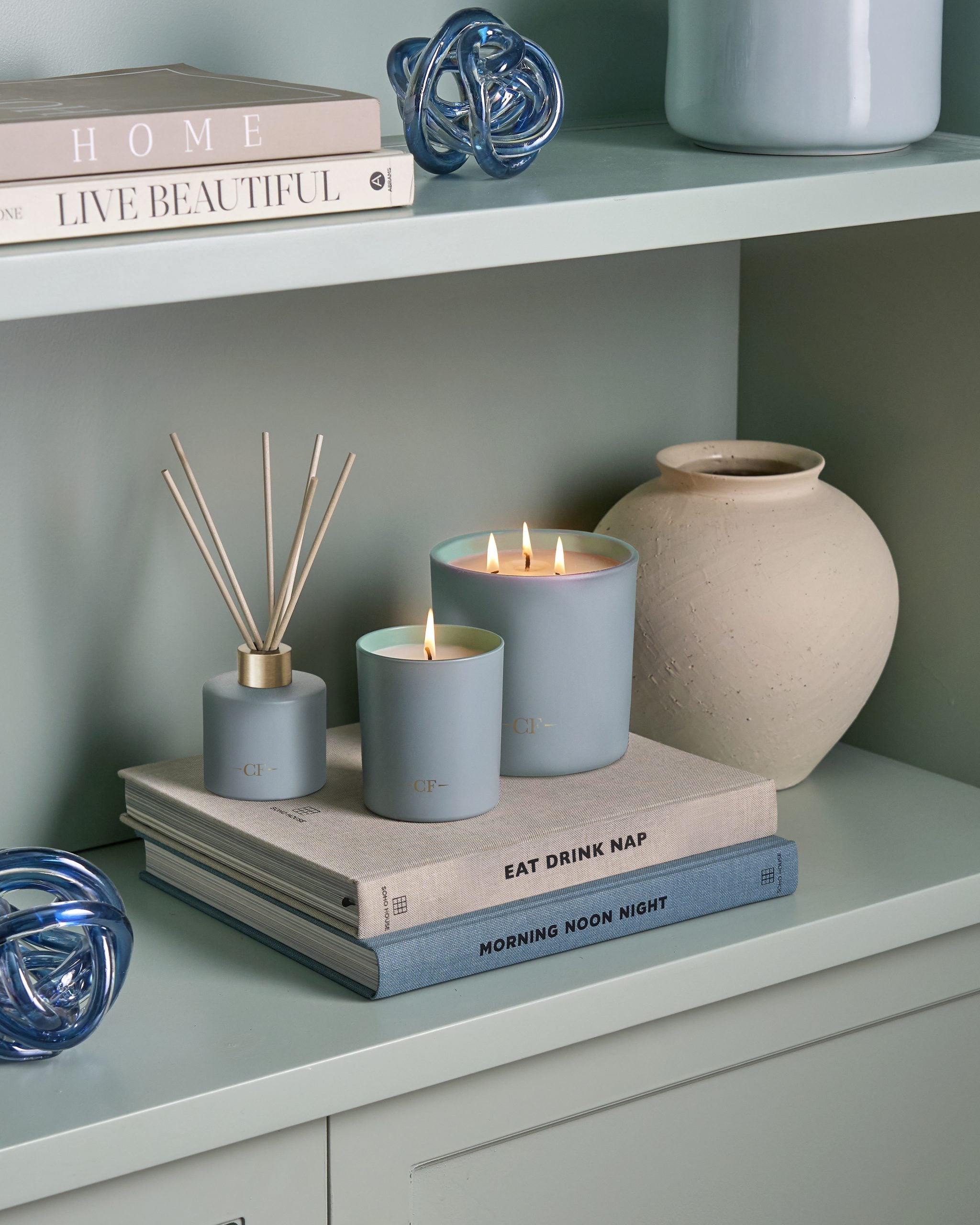 Decorative items including candles and a diffuser on a shelf with books and a vase.