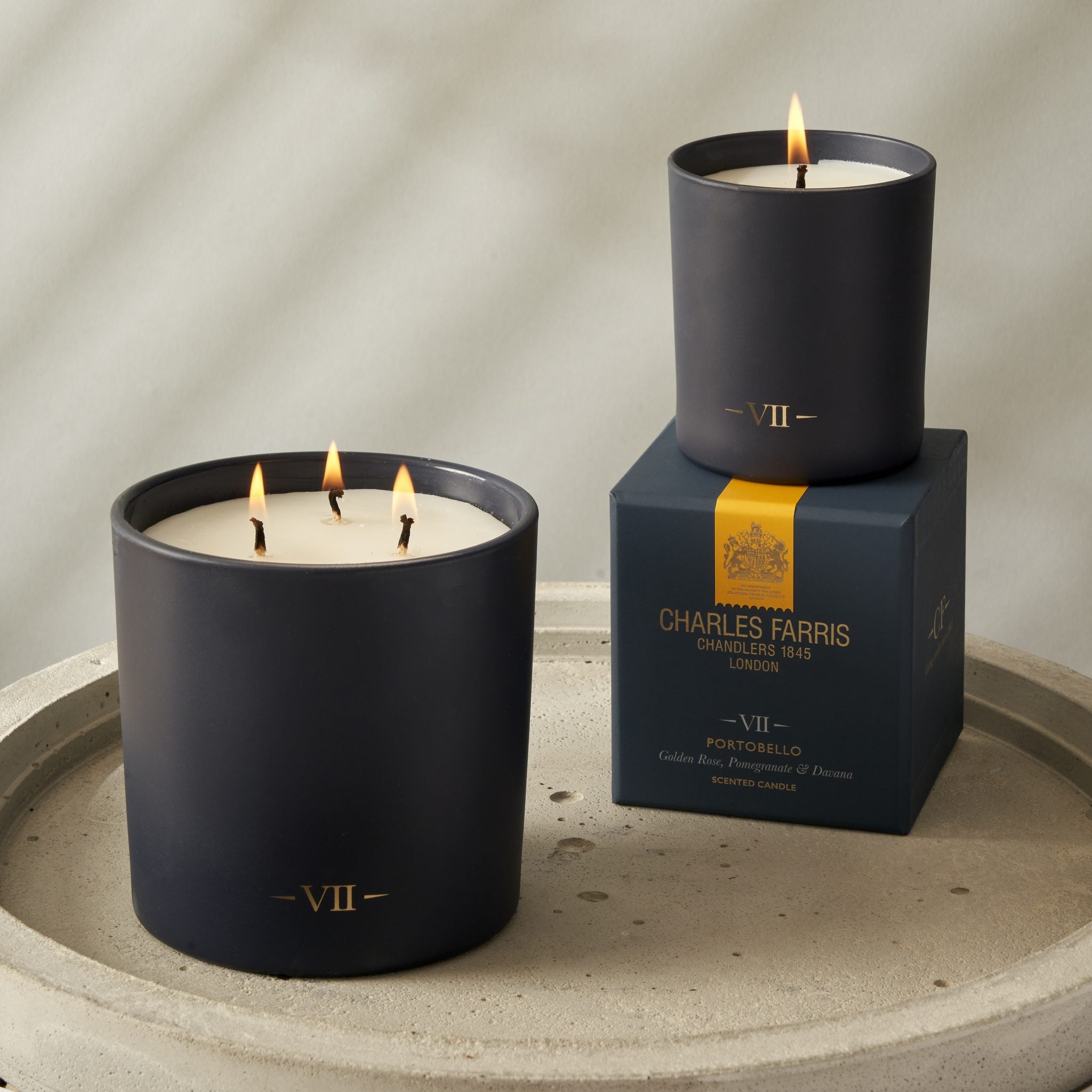 Two Charles Farris candles with 'VII' on a stone surface, with a branded box in the background.