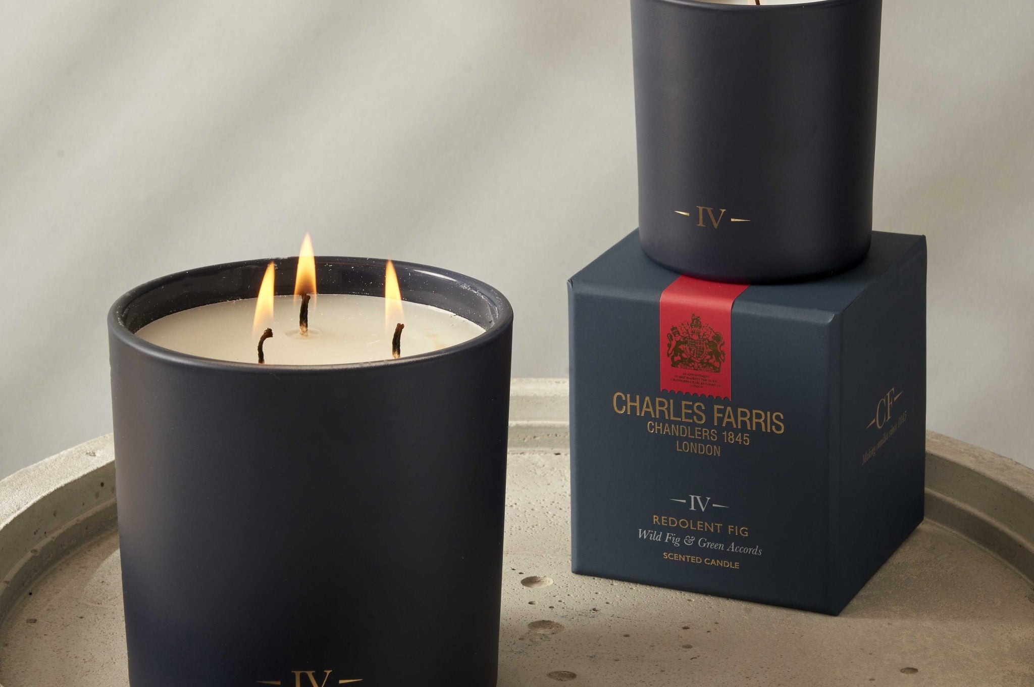 Two lit candles in black containers with a box labeled 'Charles Farris' on a stone surface.