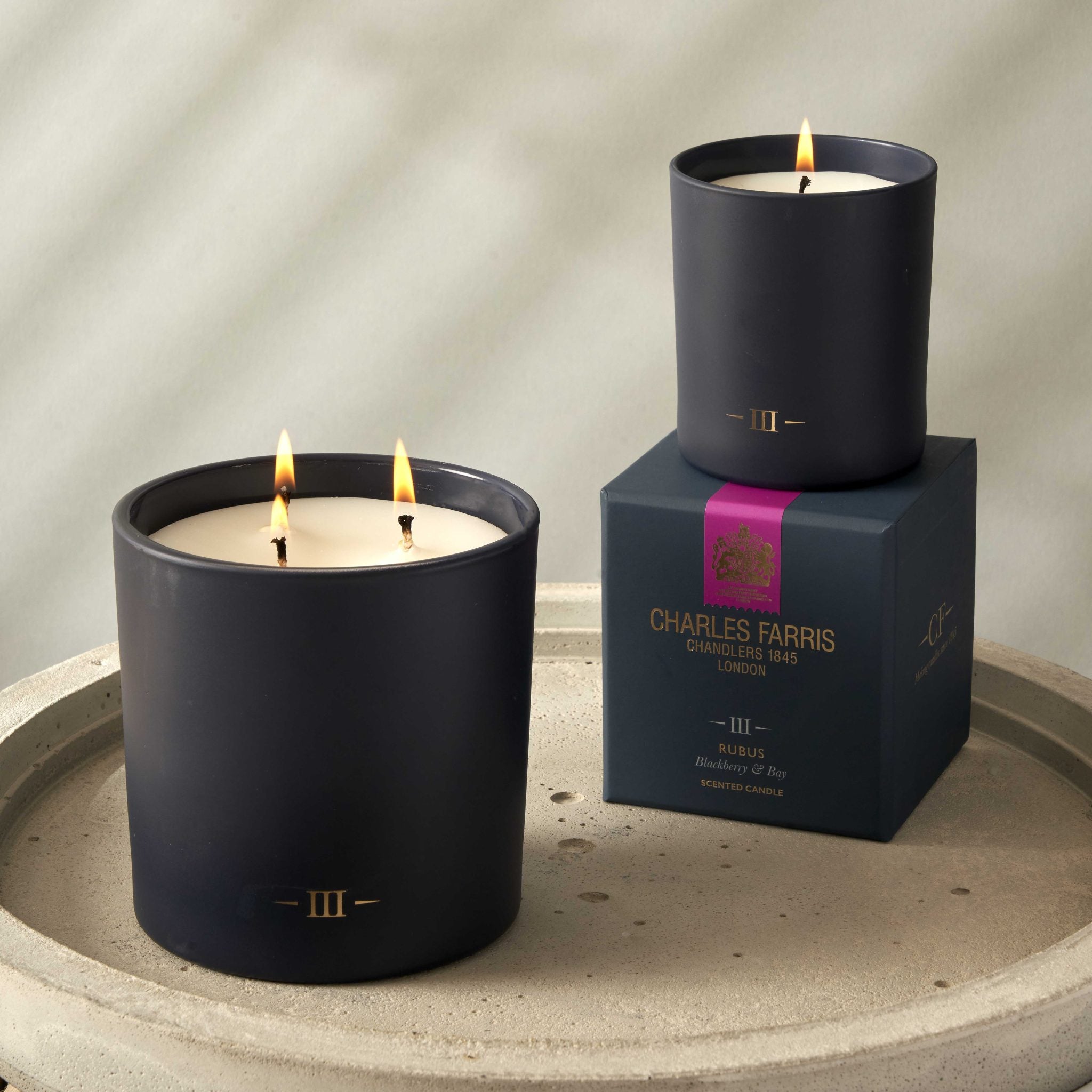 Two candles with visible flames on a stone surface, one on a box labeled 'Charles Farris'.