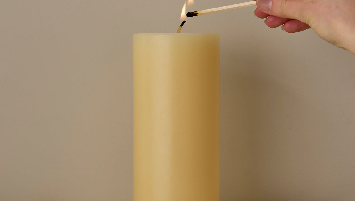 Hand lighting an ivory candle with a match on a marble surface.