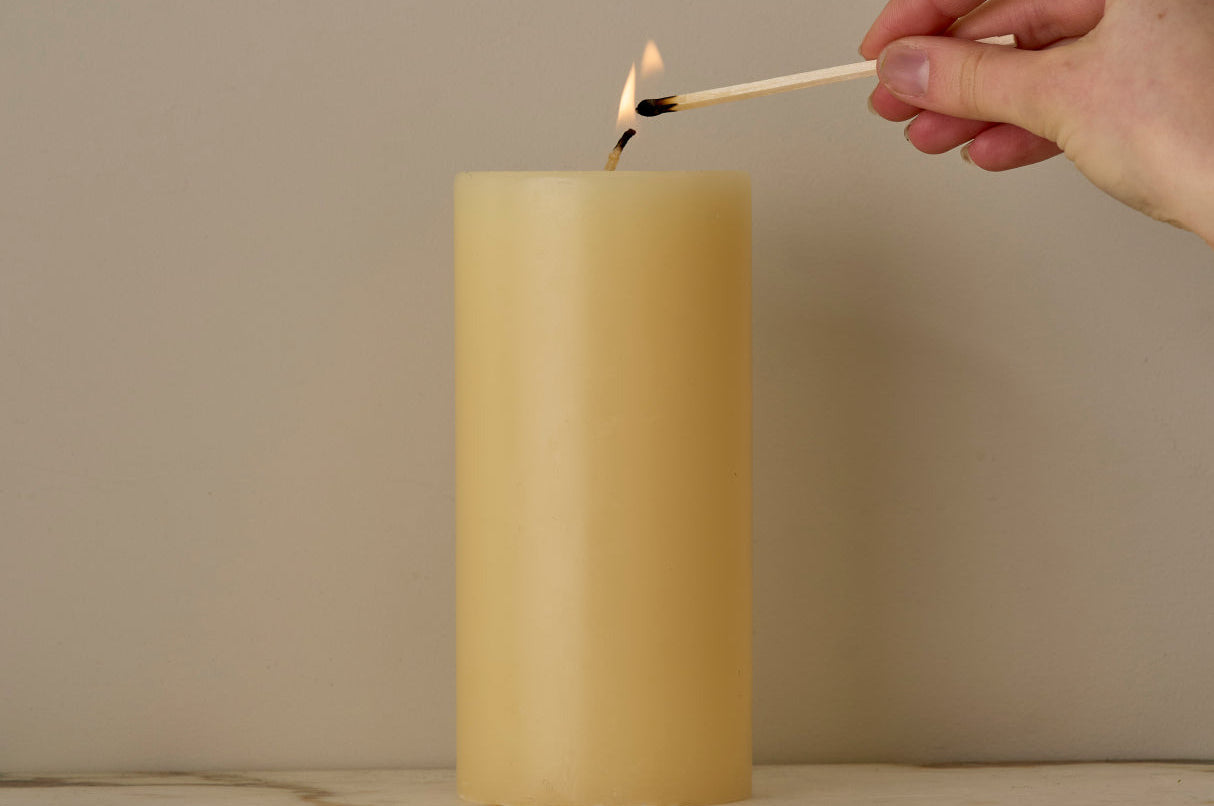 Hand lighting an ivory candle with a match on a marble surface.
