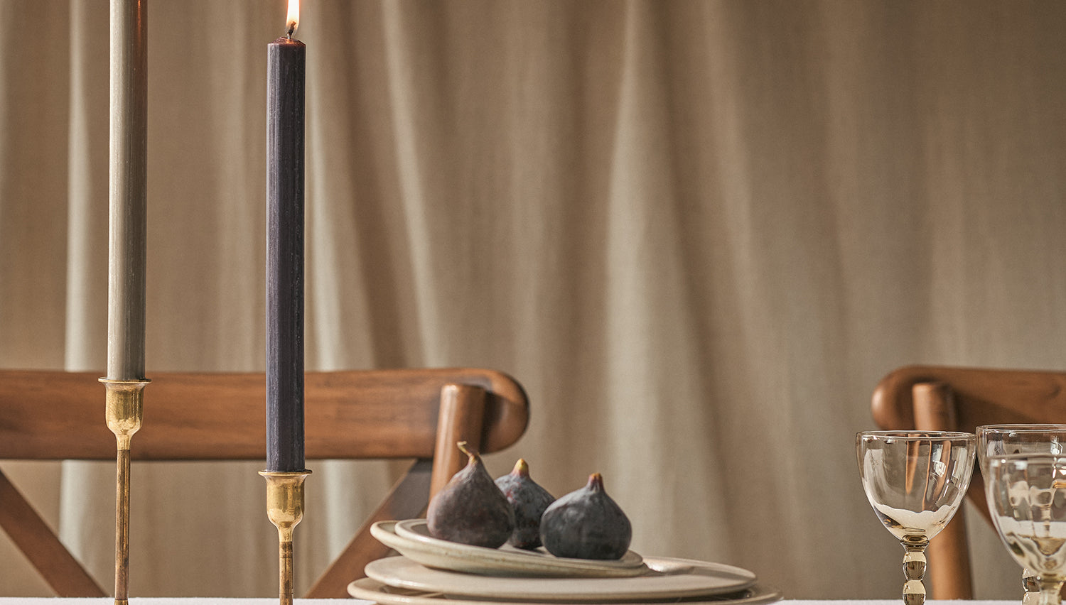 Two lit dinner candles on a table with plates