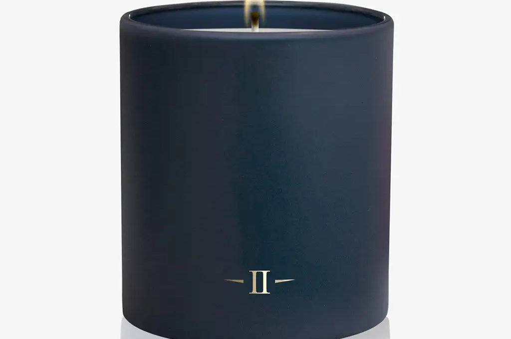 Navy blue candle with a small flame on a white background