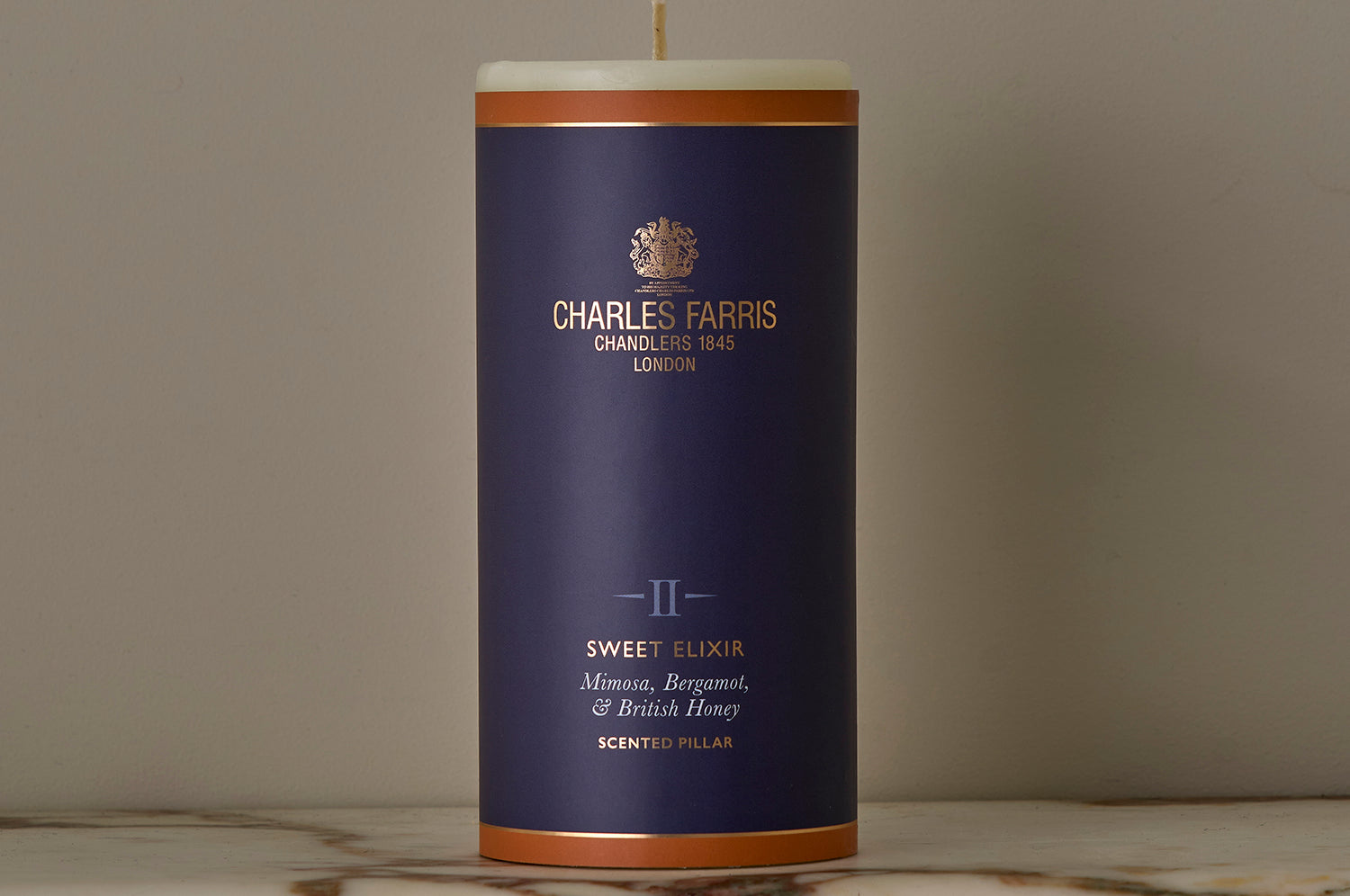 A Sweet Elixir Scented Pillar Candle on a marble surface.