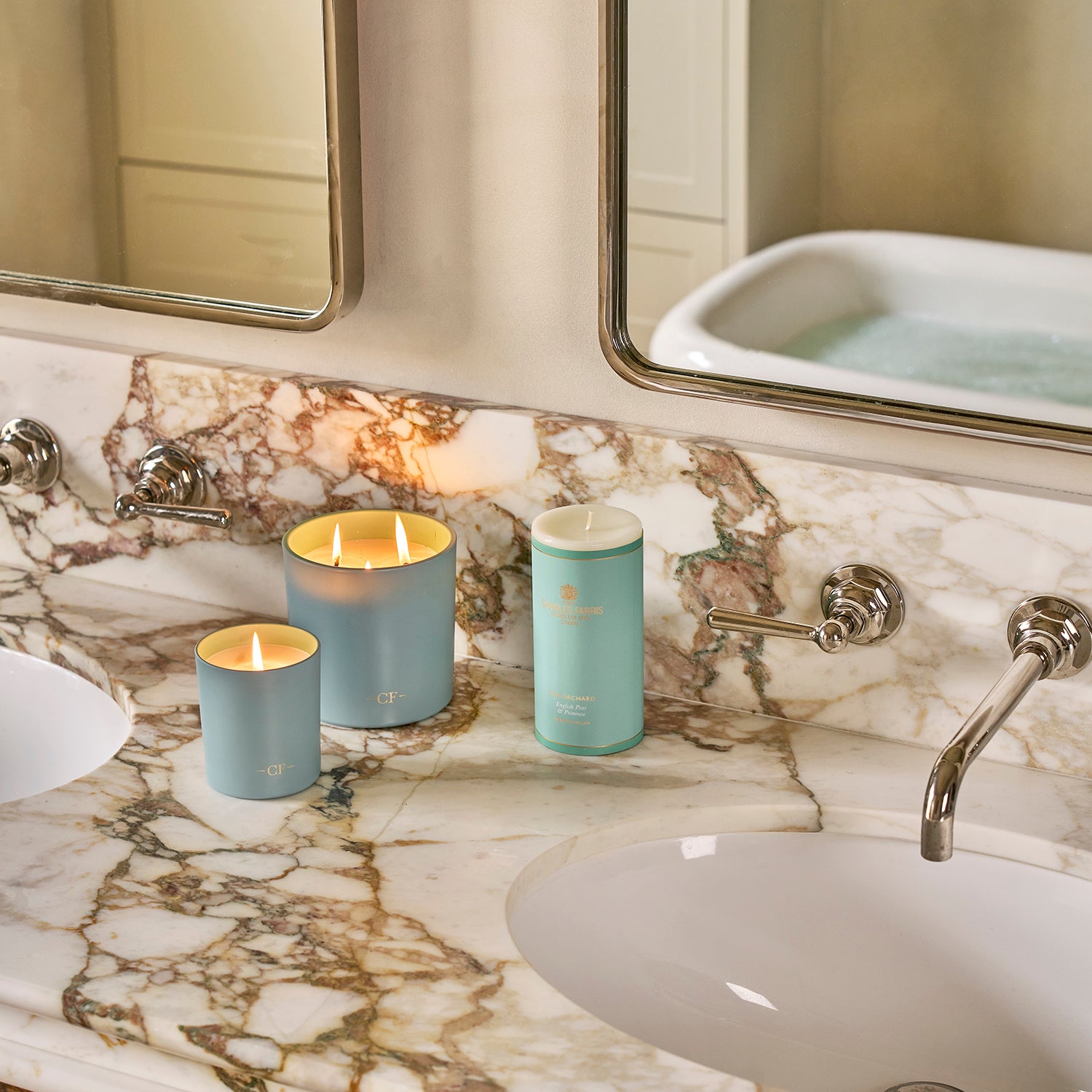Three teal candles on a marble bathroom counter with a sink and mirror in the background.