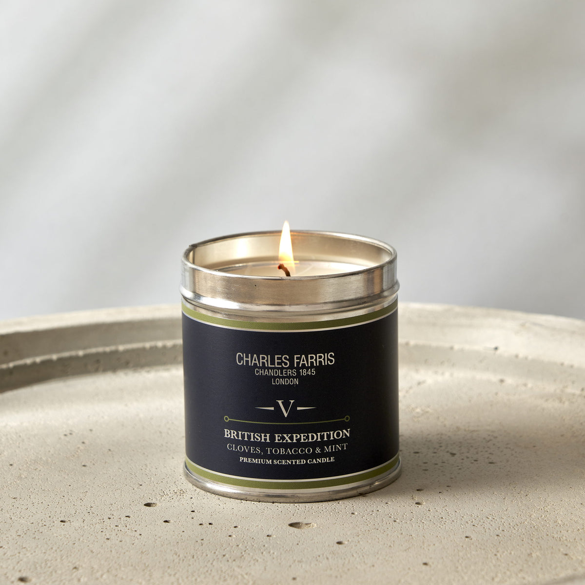 Charles Farris Grand Cascade signature tin candle burning on a concrete tray, scented with smoky cedar, moss and amber